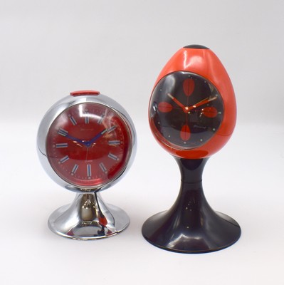 Image BLESSING 2 unusual table alarm clocks Space age from the 1970´s, Germany, manual winding, plastic housing, rear site setting for alarm, winding and hand-setting, 1x black dial with luminous points, orange luminous hands, 1x red dial with raised hour-indices and luminous dots, blue luminous hands, height approx. 20,5 and 14,5 cm, width approx. 12 and 10,5 cm, 1x mainspring has to be replaced, signs of use otherwise condition 2